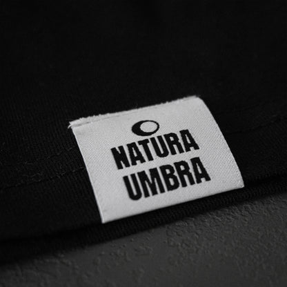 Schwarzes Unisex T-Shirt von Natura Umbra – Detailansicht des gewebten Markenetiketts am linken Saum.
