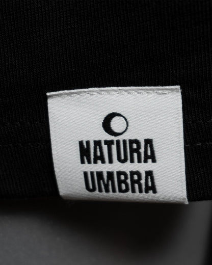 Detailaufnahme des Webetiketts am Saum des T-Shirts in Schwarz – dezentes Branding-Element von Natura Umbra.