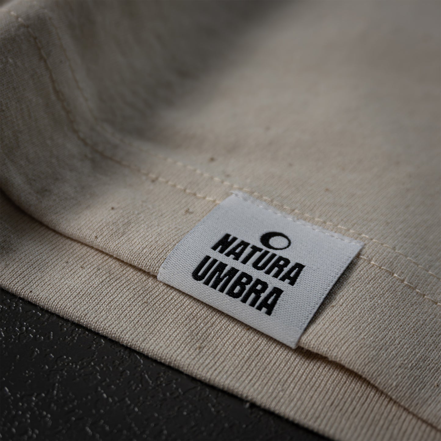 Nachhaltiges T-Shirt in Natural Raw von Natura Umbra – Detailansicht des gewebten Markenetiketts am linken Saum.