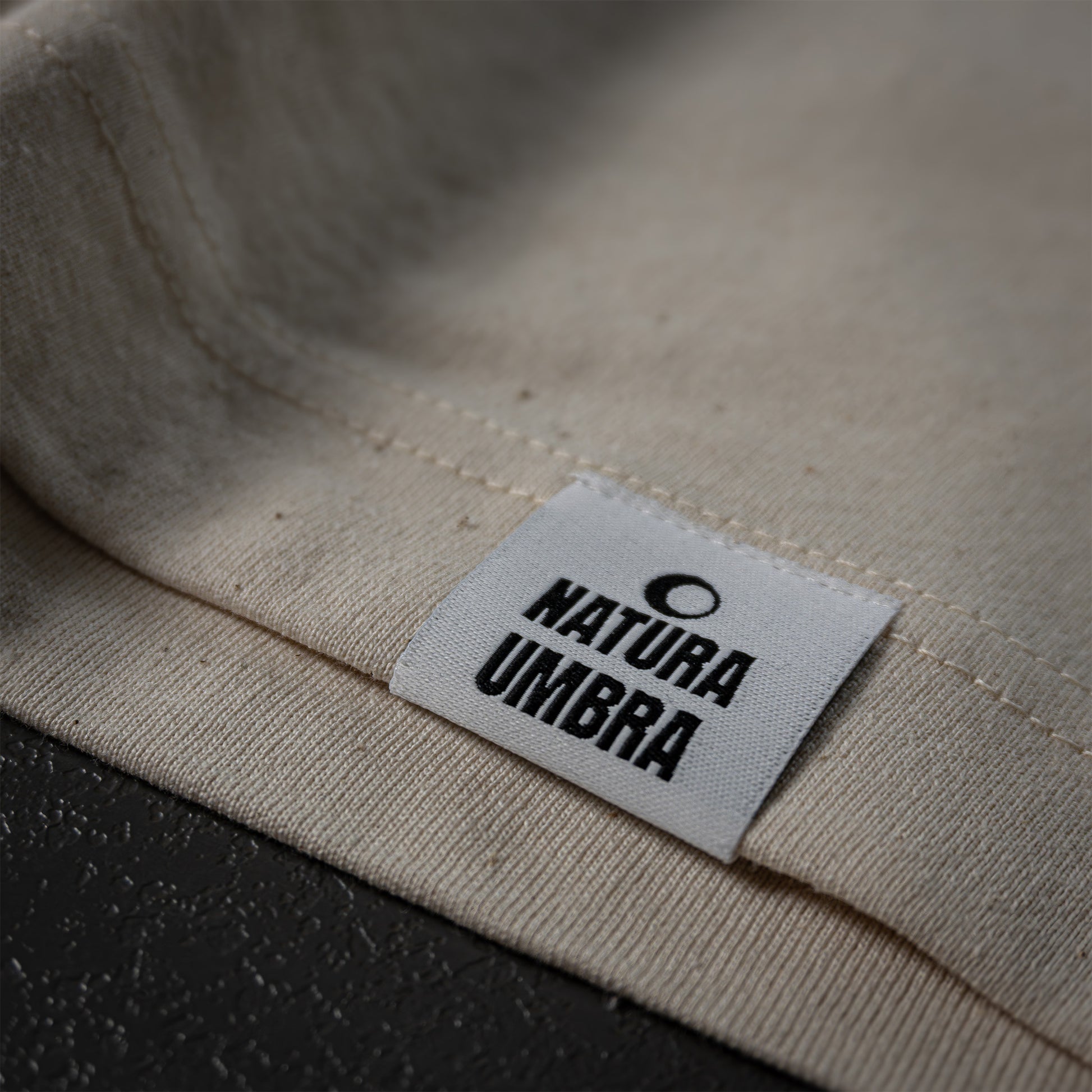 Nachhaltiges T-Shirt in Natural Raw von Natura Umbra – Detailansicht des gewebten Markenetiketts am linken Saum.